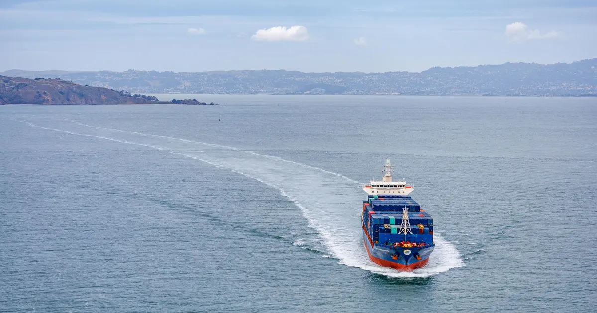 A cargo ship filled with containers travels across calm ocean waters on a clear day.