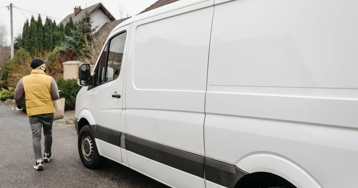 A delivery person carrying a package away from a delivery van outdoors, showcasing efficient logistics.