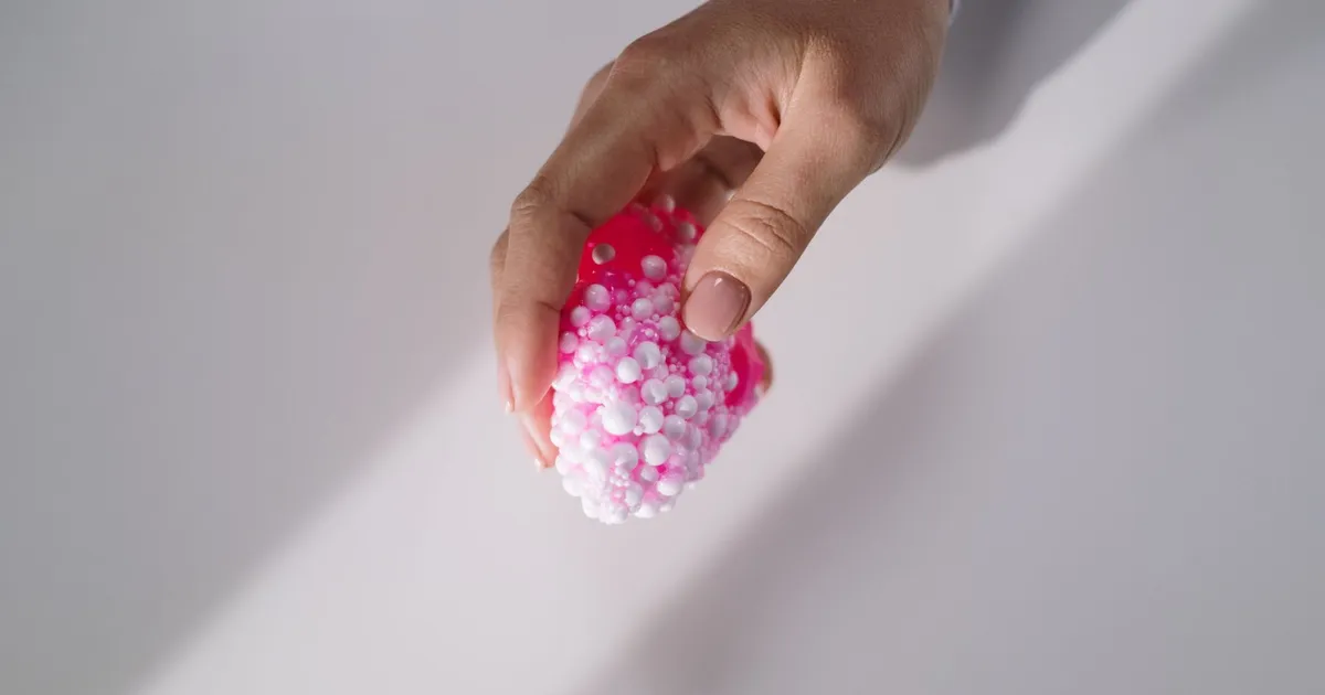 A hand gently holds a pink textured slime with small foam beads, showcasing tactile sensation.