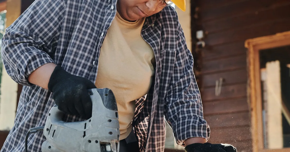 A focused construction worker using an electric jigsaw on wood outdoors.