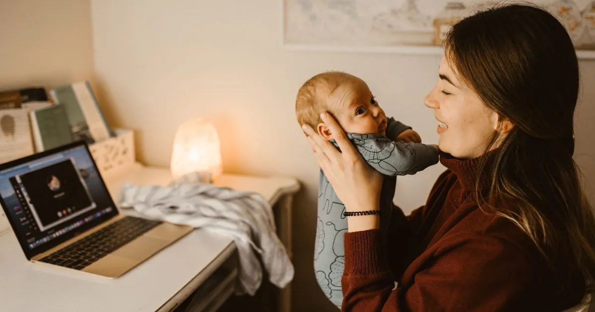 Mother holding baby while video calling from home office. Cozy and heartwarming indoor scene.
