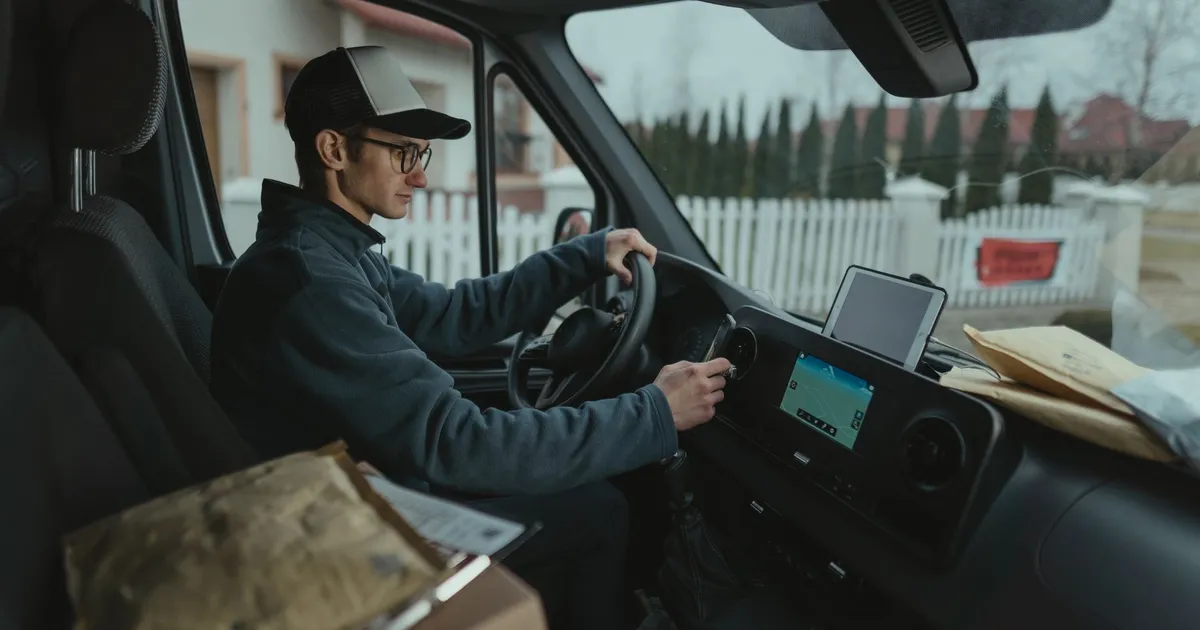 Courier driving van with packages, using GPS for efficient delivery route.