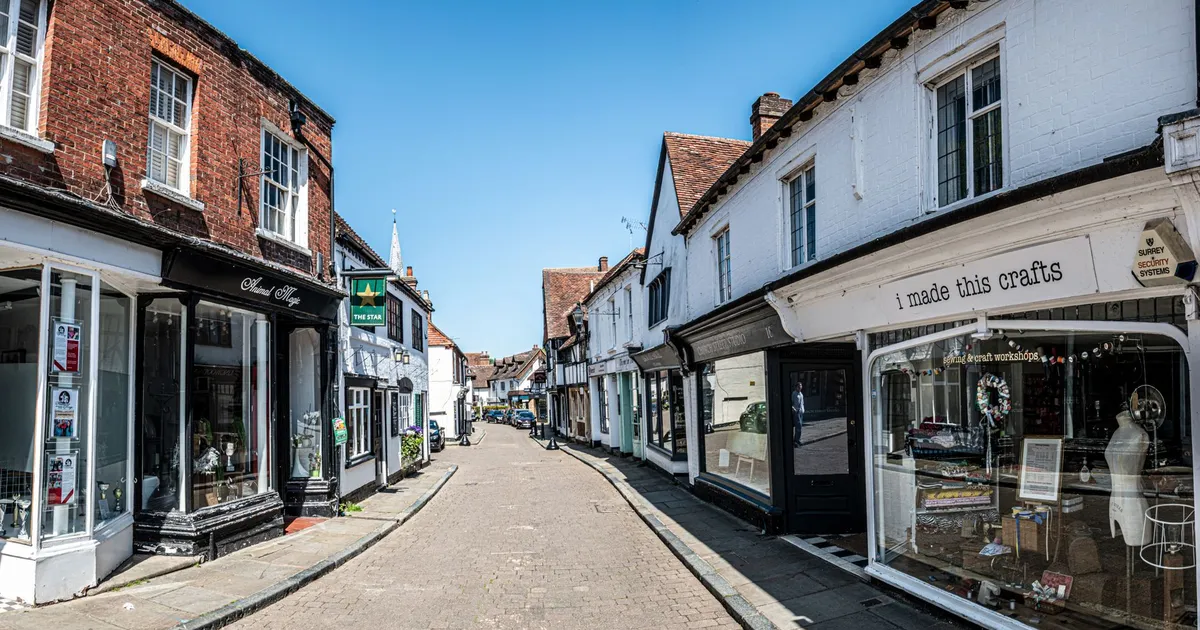 Picturesque view of an empty street in historic Godalming, England with old shops and blue sky.