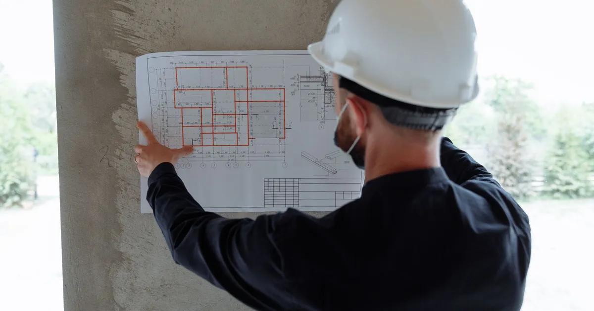 Engineer in hardhat reviewing architectural floor plans at construction site.