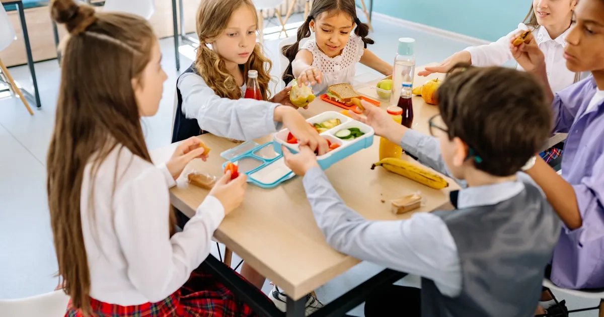 Group of diverse children having lunch in a school canteen, sharing and enjoying healthy snacks.