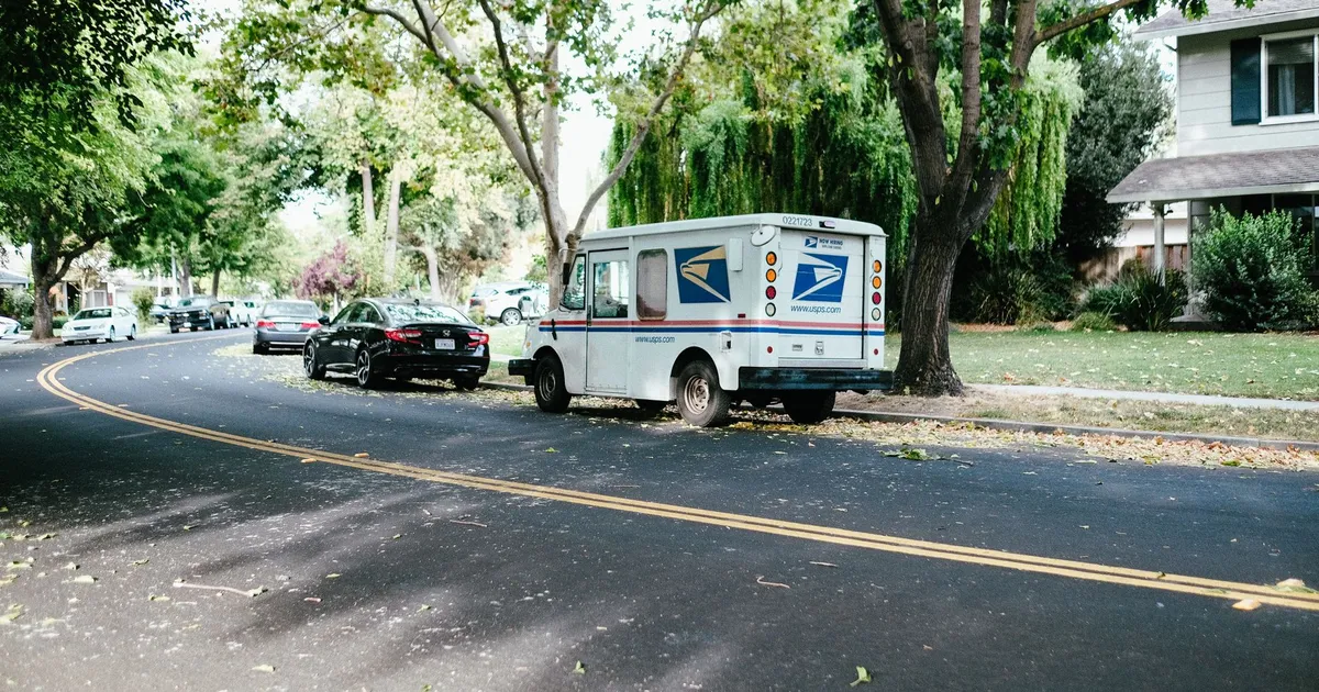 A postal delivery van parked on a tree-lined suburban street, showcasing daily mail service.