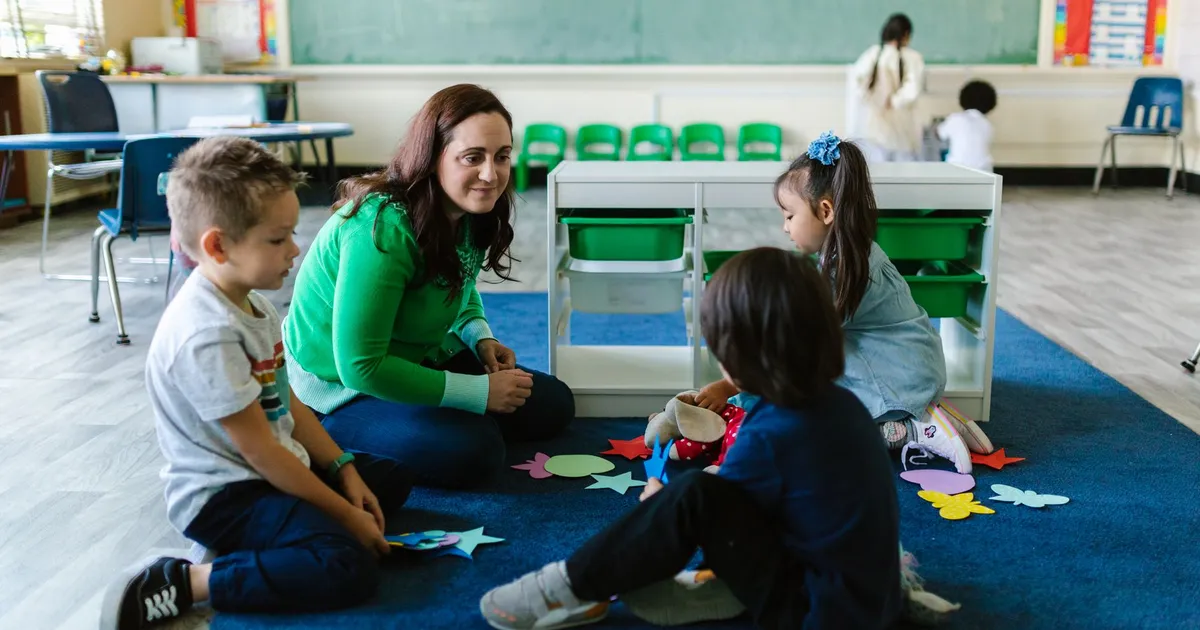 Teacher and children engaged in educational activities on a classroom floor.