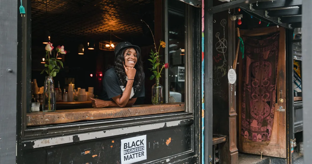 A cheerful businesswoman leaning out of her café window, showcasing a black-owned business with vibrant flowers and decor.