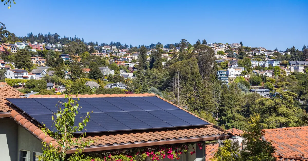 Solar panels on a suburban home, surrounded by lush greenery and a sunny blue sky.