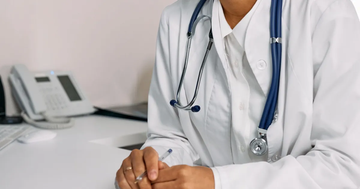 Doctor with stethoscope and white coat seated at a clinic desk.