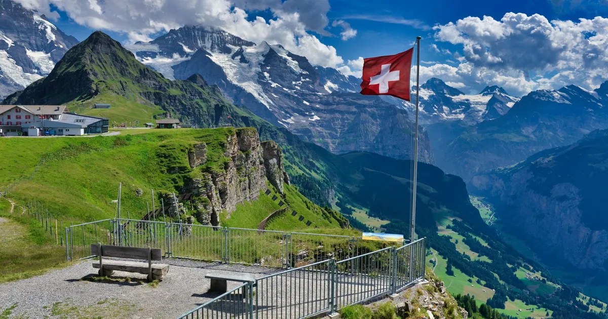 Breathtaking panoramic view of Swiss Alps from Grindelwald with iconic Swiss flag and lush green landscape.