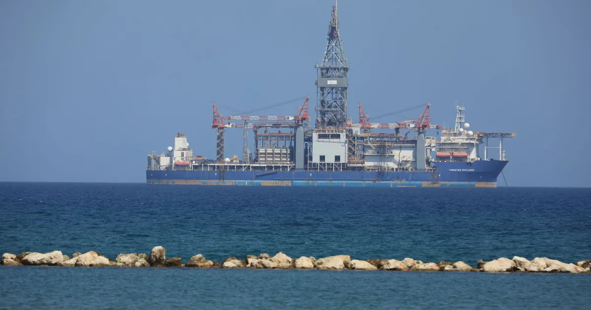An offshore drilling rig floats on a calm sea with a clear blue sky in the background.