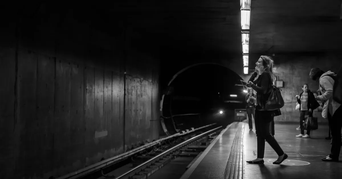 Monochrome image of commuters waiting on a dimly lit subway platform, showcasing urban life.