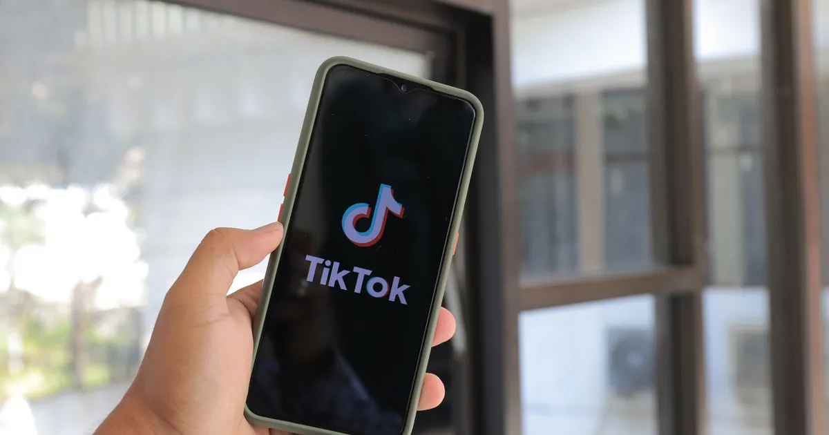 Close-up of a hand holding a smartphone displaying the TikTok app indoors.