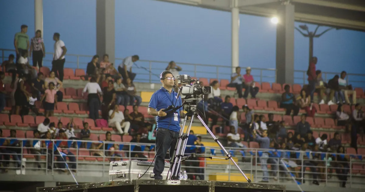 Cameraman on platform capturing footage at crowded stadium event.
