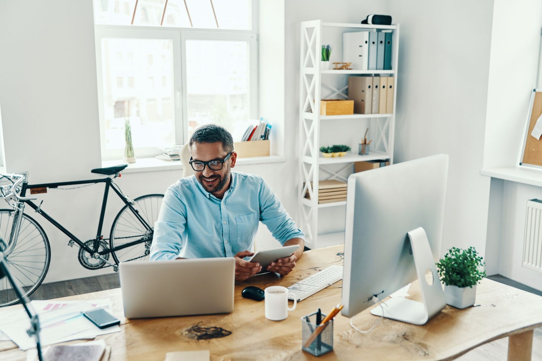 Man smiling while working on a laptop and using digital devices in a modern workspace.