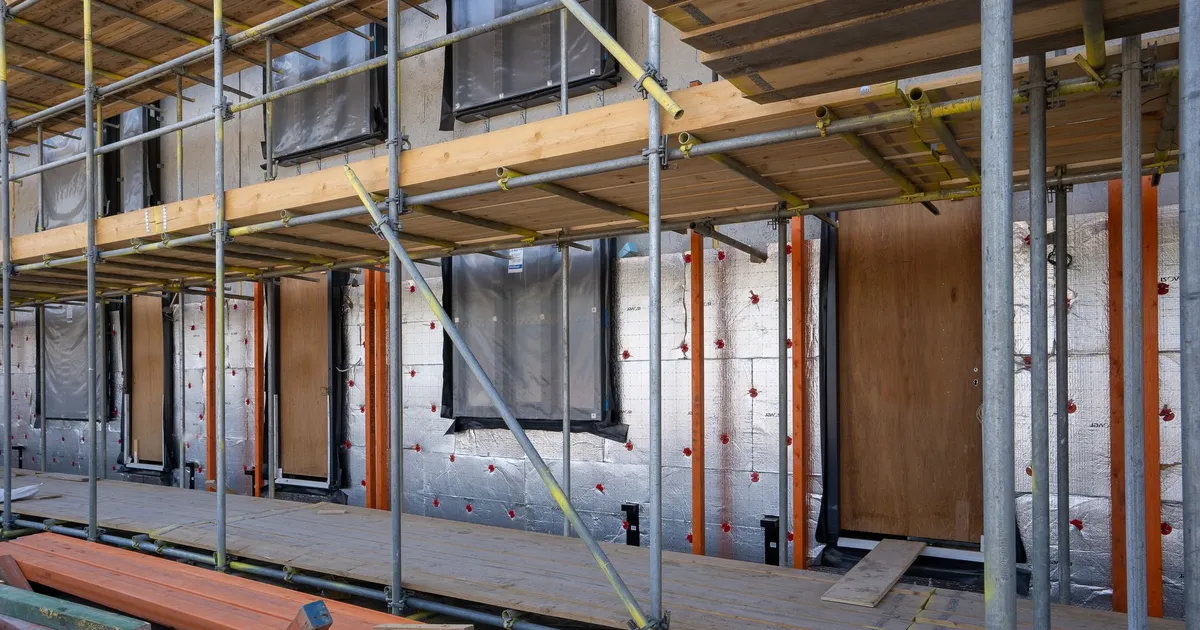 Scaffolding at a residential building under construction with windows and insulation sheets visible.