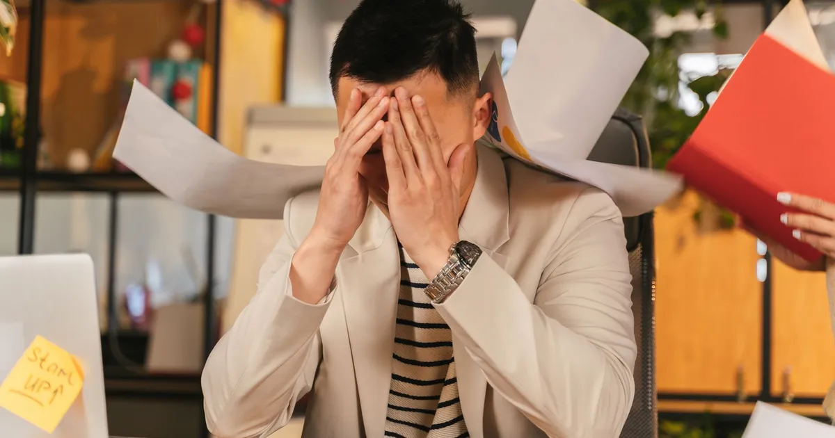 Stressed businessman overwhelmed by paperwork in office environment, demonstrating burnout.