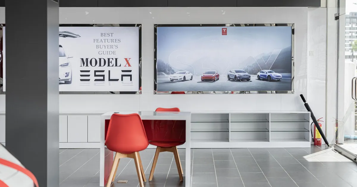Spacious car dealership interior featuring red chairs and advertising displays with electric cars.