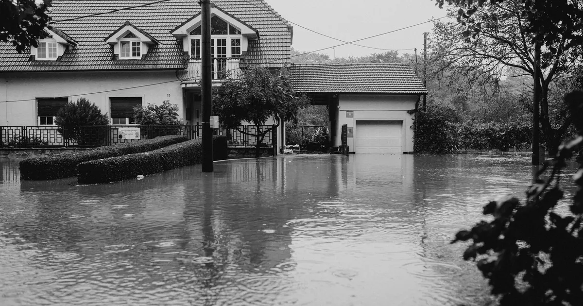A flooded suburban house surrounded by high water, depicting severe weather impact.