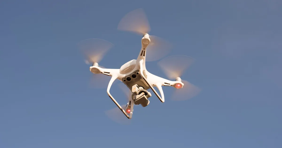 A white drone in flight against a clear blue sky, capturing aerial footage with precision.