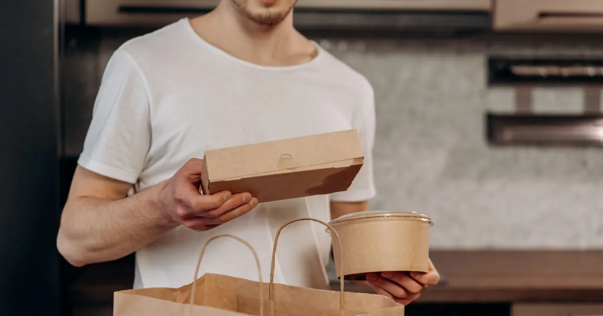 A man in a white shirt manages takeaway food in a kitchen, emphasizing convenience and modern lifestyle.