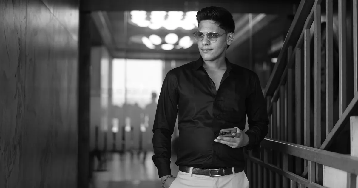 Fashionable man standing indoors with a confident pose, captured in black and white for modern aesthetic.