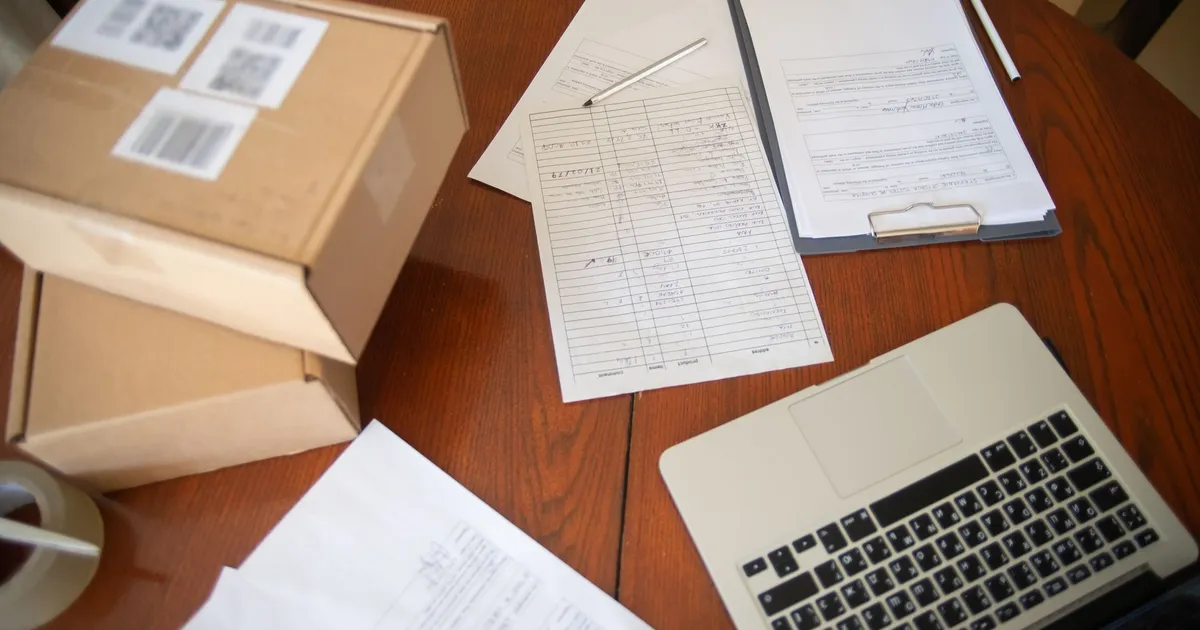 Flat lay of a workspace with laptop, documents, and cardboard boxes for e-commerce operations.