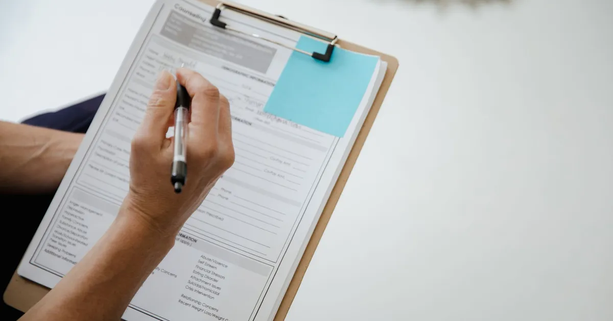 A person writes on a document using a clipboard indoors.