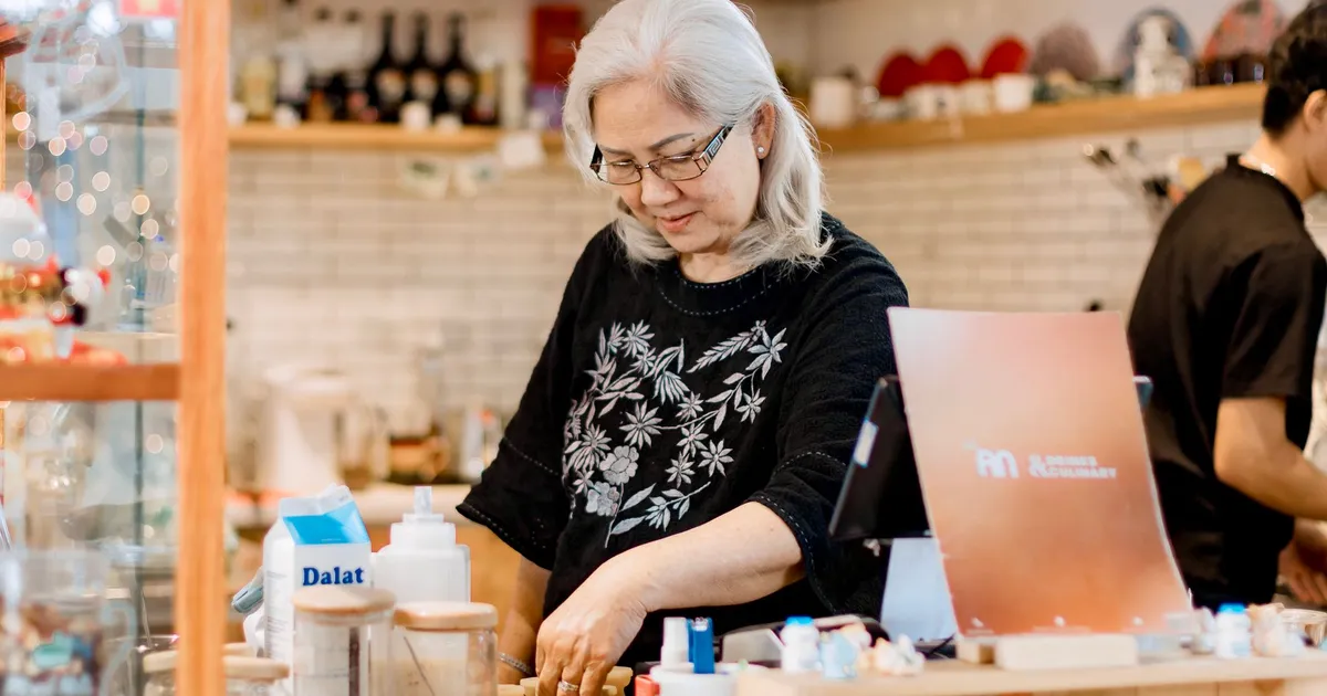 Senior woman working behind the counter in a cozy, warmly lit coffee shop.