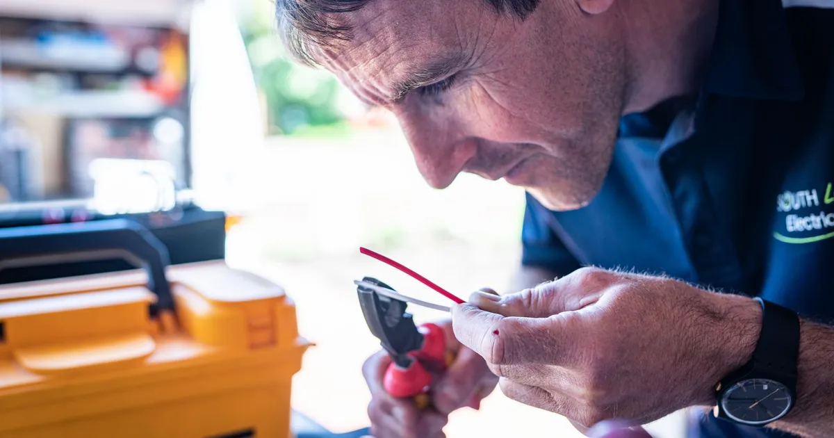 Focused technician working on wiring with tools in a workshop setting.