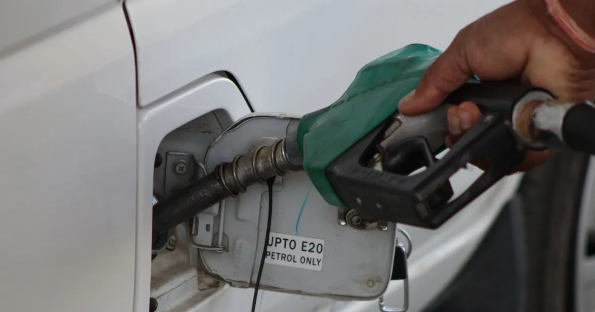Hand refueling car with E20 petrol at a gas station, close-up view.