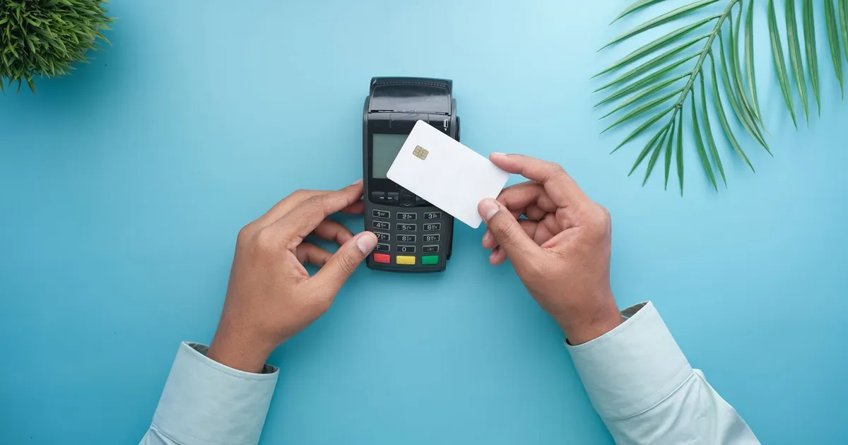Hands using a contactless credit card on a payment terminal with a stylish minimal background.