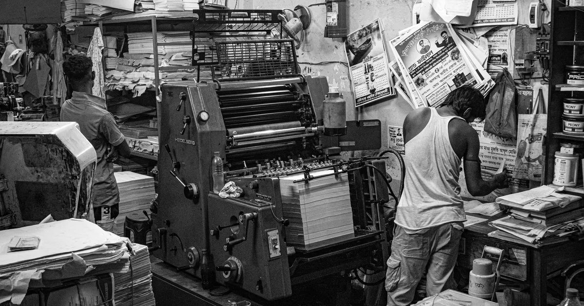 Black and white image of a bustling print shop with workers operating a printing press.