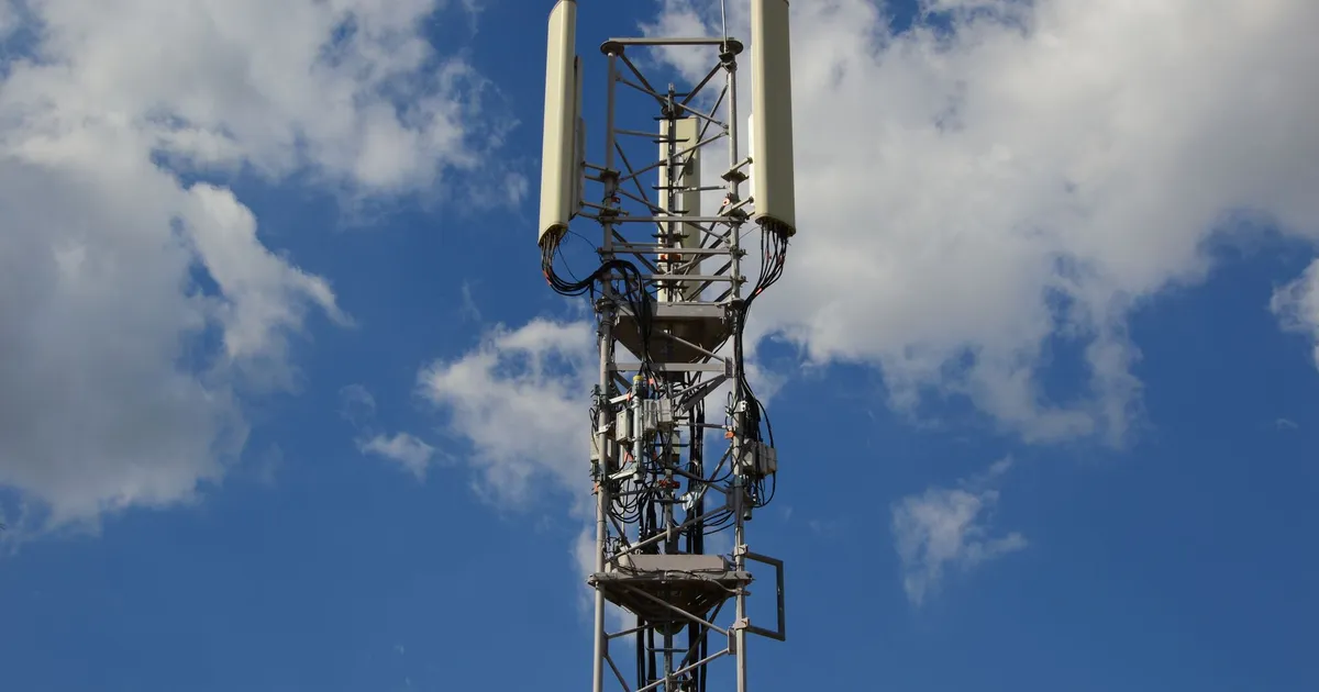 A tall cellular communication tower against a vivid blue sky, symbolizing modern technology.