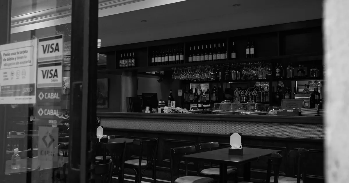 A black and white view of a cozy bar interior with empty seating and a well-stocked counter.