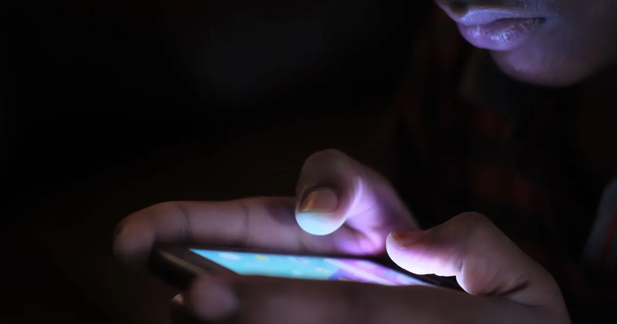 Close-up of a person holding and using an illuminated smartphone in a dark setting.