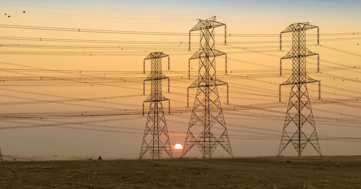 Three electricity pylons silhouetted against a vibrant sunset in open landscape.