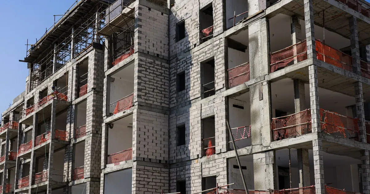A modern multi-story apartment building under construction with scaffolding and safety netting.