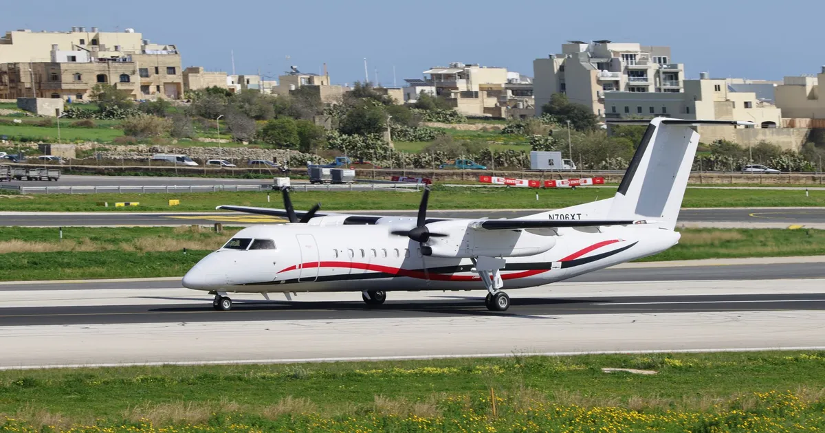 A turboprop airplane taxis on the runway with urban buildings in the background.
