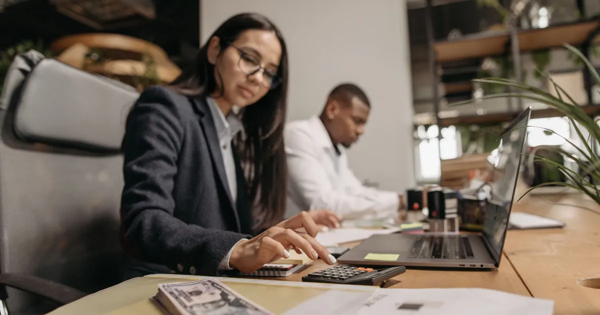 Two business professionals collaborating with a laptop and calculator in a modern office.