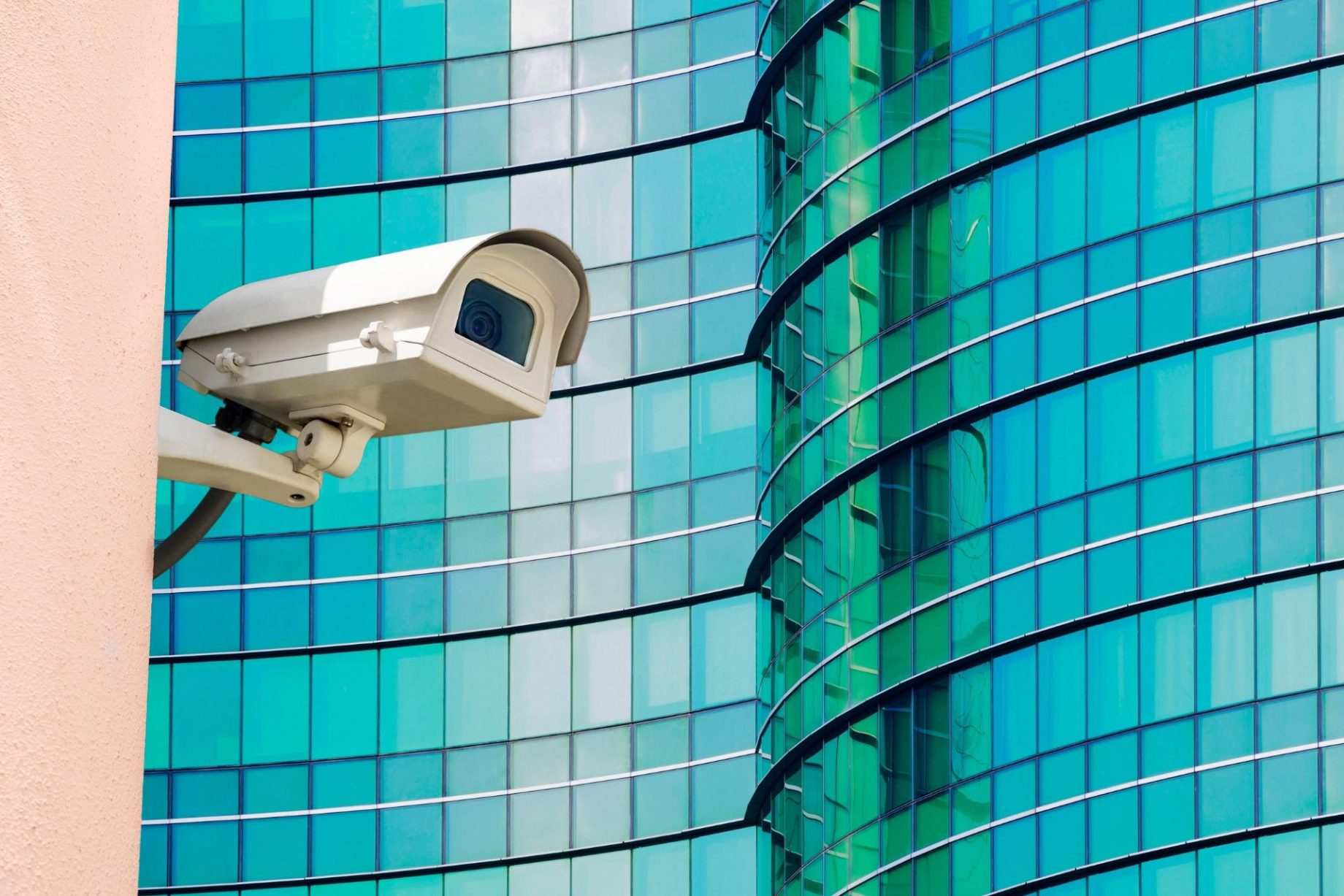 Security camera mounted on a modern glass office building monitoring the workplace exterior
