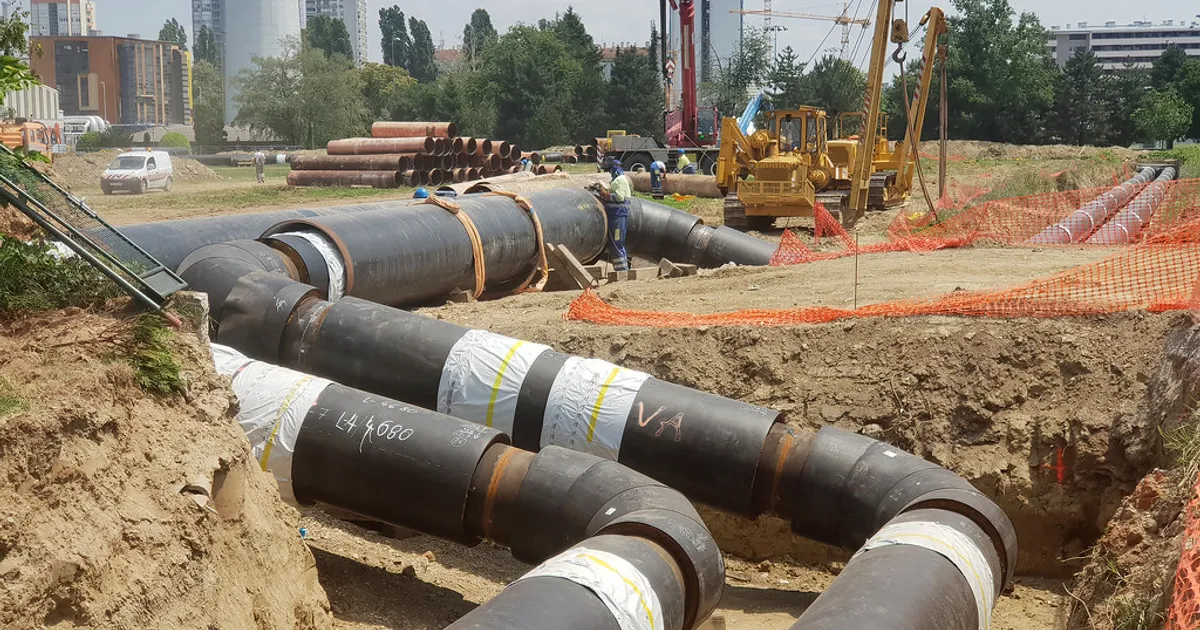 Laying heating pipes in a trench at construction site.
