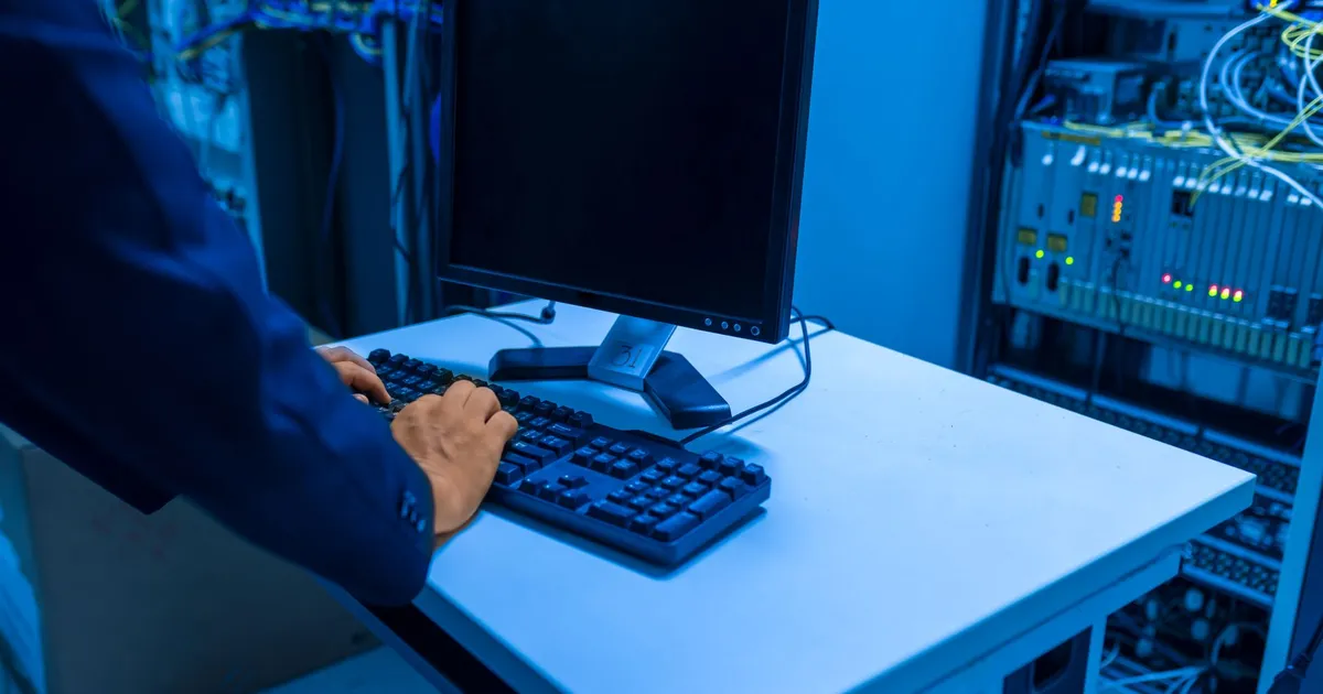 An IT professional operates a computer in a server room, managing network systems and connected devices.
