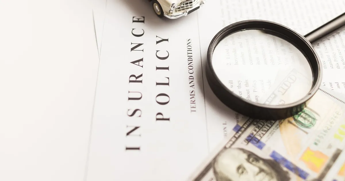 Close-up image of an insurance policy with a magnifying glass, money, and toy car.