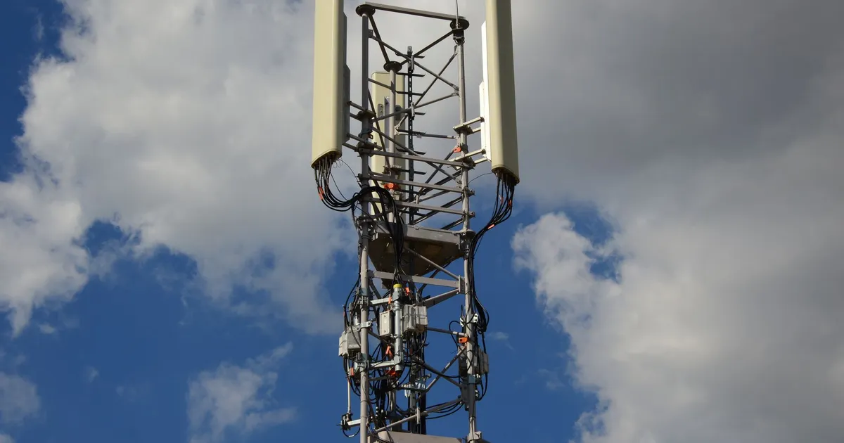 High-angle view of a modern cell tower with technology components against a blue sky with clouds.