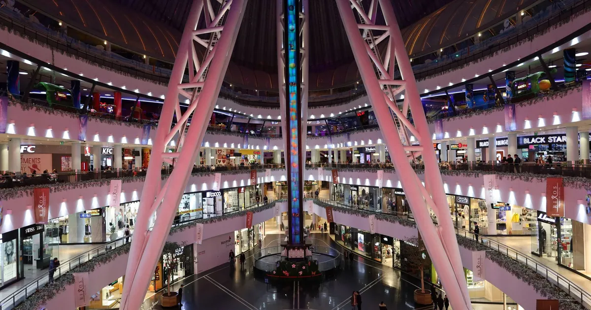 A vibrant and spacious modern shopping mall with various shops and people bustling around.