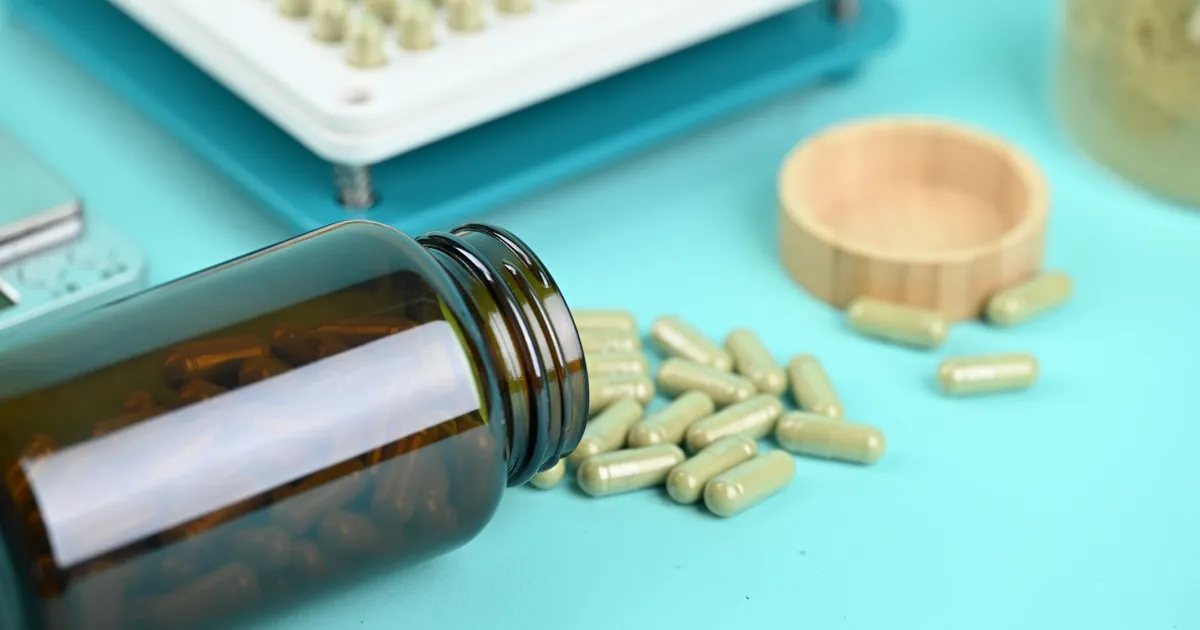 Pills and a capsule filling machine on a blue background, showcasing supplement production.