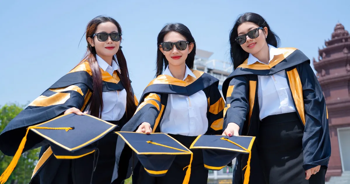 Three female graduates in gowns holding caps in celebration outdoors on a sunny day.