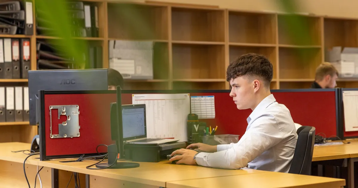 A focused young man typing on a computer in a contemporary office environment.